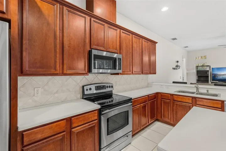The spacious Kitchen offers ABUNDANT CABINETRY and counter space, a large ISLAND WITH BREAKFAST BAR, sleek backsplash, TWO PANTRY CLOSETS and stainless steel appliances including a NEW REFRIGERATOR (2026), NEW DISHWASHER (2026) and NEW MICROWAVE (2025).