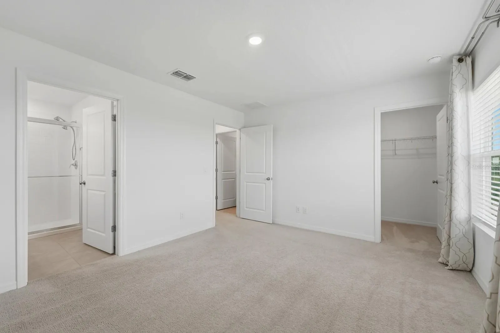 Primary bedroom with carpet flooring, walk-in closet, and direct access to the en-suite bathroom