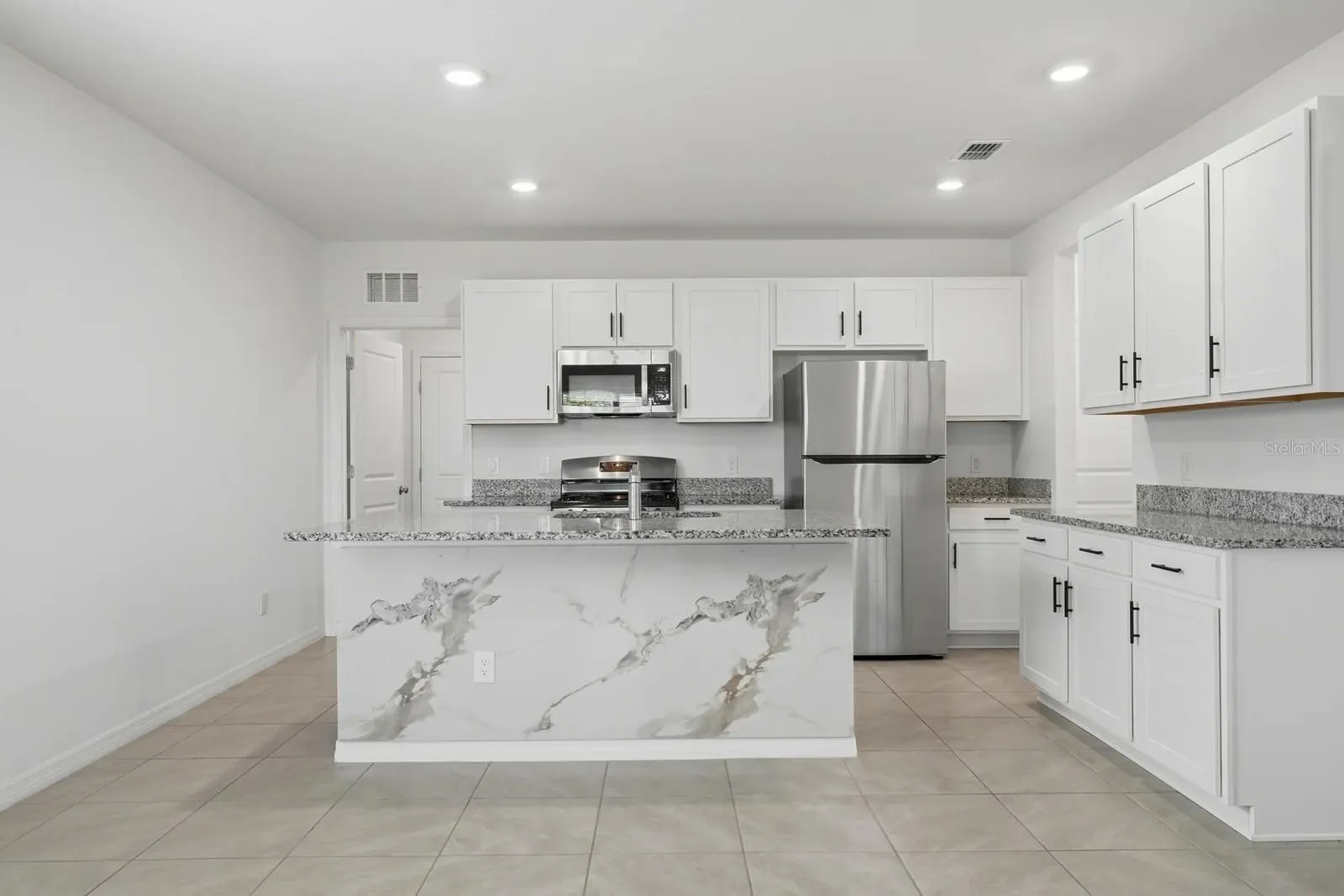 Bright kitchen featuring white cabinetry, granite countertops, stainless steel appliances, a spacious island, and a decorative stone-look accent panel