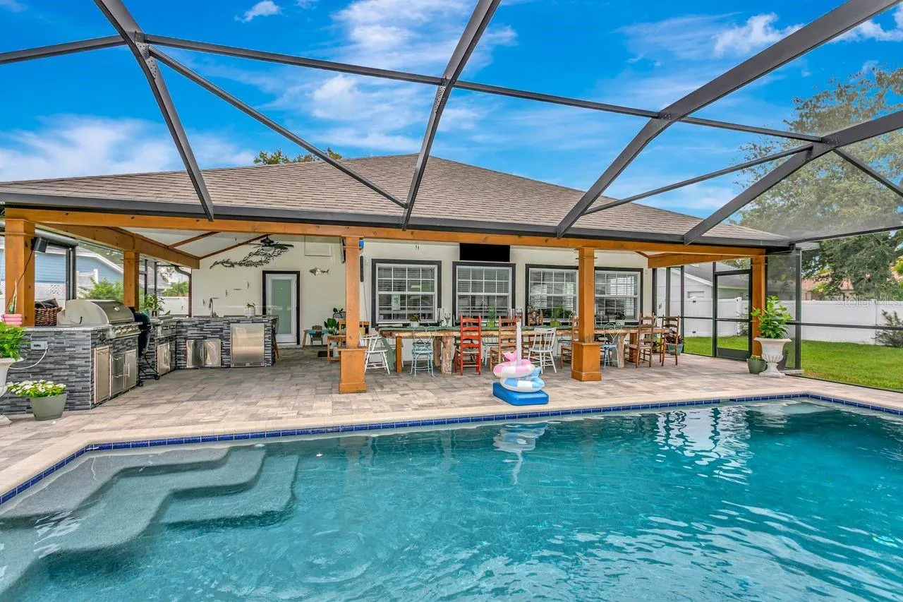 View of Outdoor Summer Kitchen; Expansive Covered Rear Lanai; Custom Pool with Sun Shelf, Fire and Waterfall feature; Pavered Floor; Additional Seating Areas; and Electric Sunshades