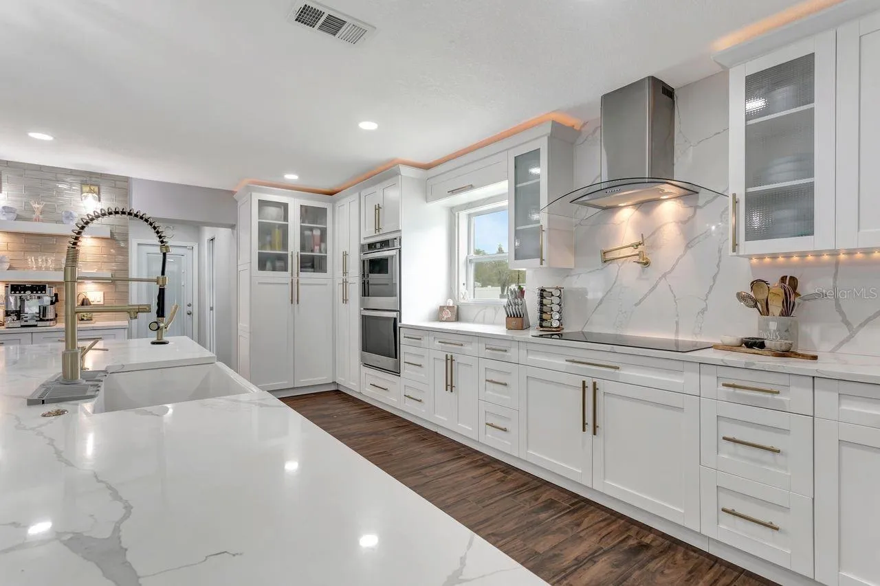 Remodeled Kitchen with upgraded custom cabinets with crown molding trim and lighting; elevated hardware and fixtures; quartz countertops; two-tone Cabinets; Stainless Steel Appliances with Luxury Side by Side Refrigerator; Pot Filler; Expansive Island with 2 Refrigerators and Power; Recessed & Pendant Lighting; LVP Floors and more!