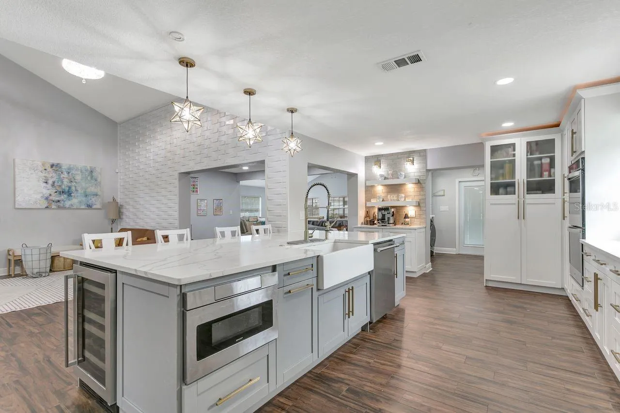 Remodeled Kitchen with upgraded custom cabinets with crown molding trim and lighting; elevated hardware and fixtures; quartz countertops; two-tone Cabinets; Stainless Steel Appliances with Luxury Side by Side Refrigerator; Pot Filler; Expansive Island with 2 Refrigerators and Power; Recessed & Pendant Lighting; LVP Floors and more!