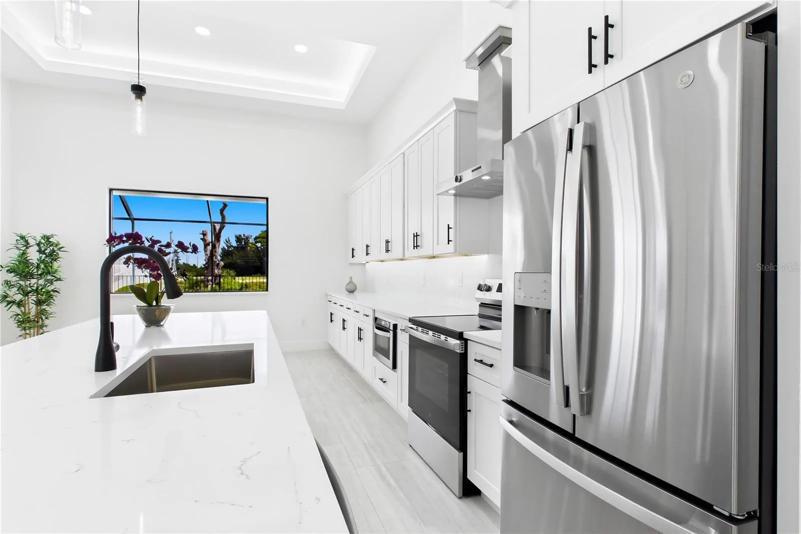 CHEF’S KITCHEN showcases expansive QUARTZ SURFACES, floor-to-ceiling WHITE SHAKER CABINETRY, matte-black fixtures &amp; stainless-steel appliances beneath a dramatic LED-LIT TRAY CEILING.