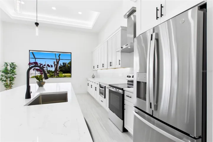 CHEF’S KITCHEN showcases expansive QUARTZ SURFACES, floor-to-ceiling WHITE SHAKER CABINETRY, matte-black fixtures &amp; stainless-steel appliances beneath a dramatic LED-LIT TRAY CEILING.
