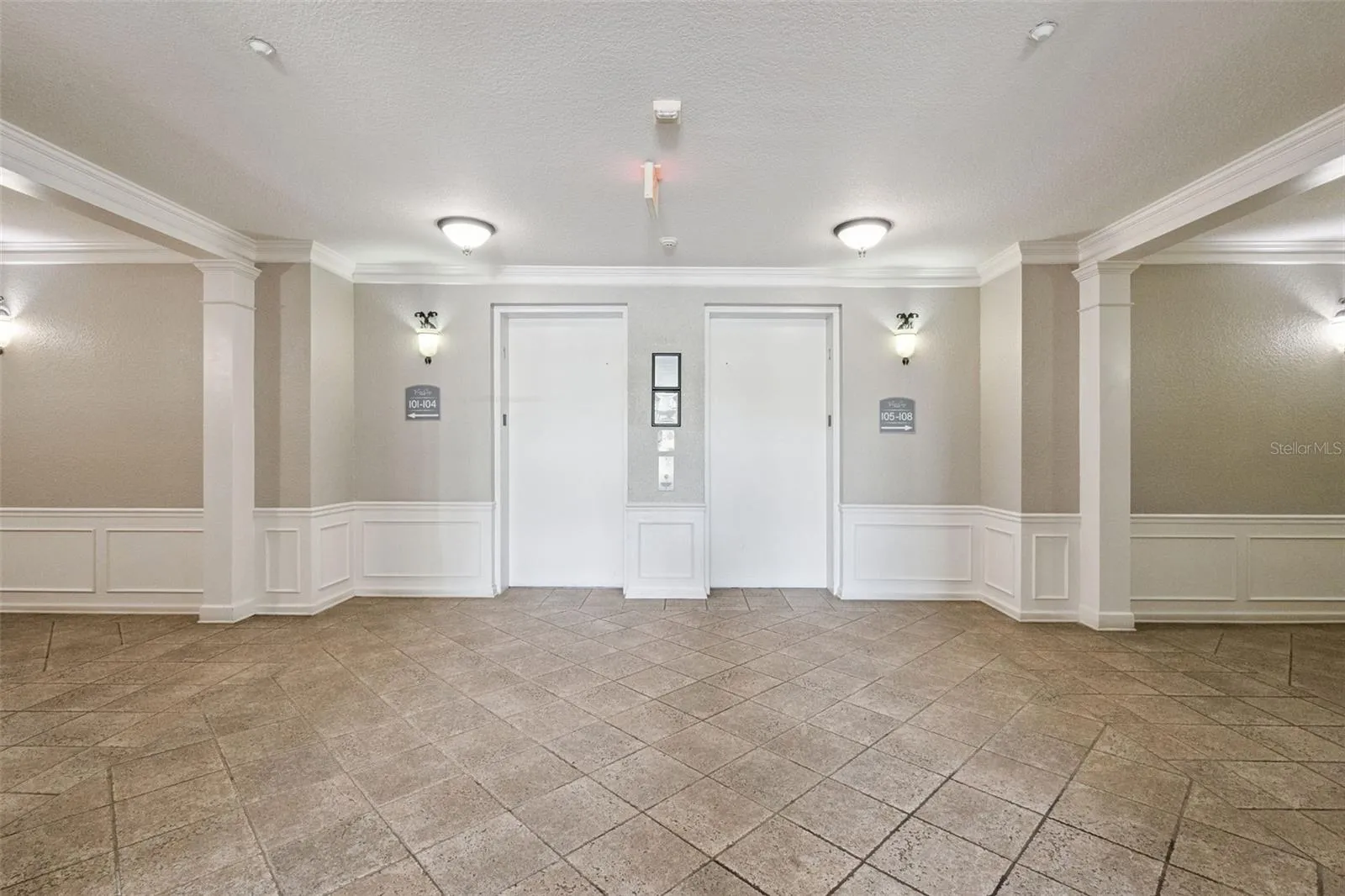 Elevator Lobby:Spacious interior building lobby featuring tiled flooring, classic wainscoting, warm wall sconces, and dual elevator access.