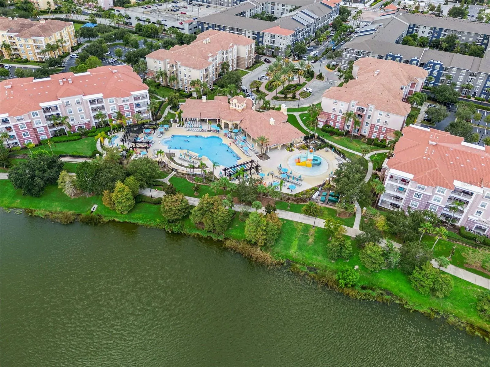 Pool & Clubhouse Aerial:High-angle aerial view highlighting the resort-style pool, kids' splash park, clubhouse amenities, and lakefront walking path.