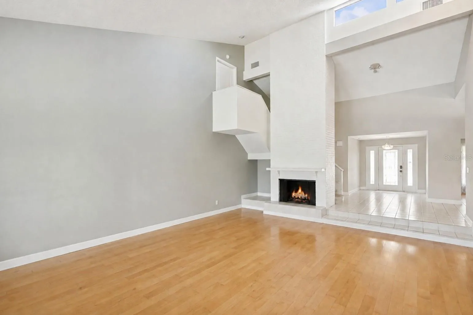 Inviting foyer and family room featuring a floor-to-ceiling brick fireplace, skylights that fill the space with natural light, and a staircase leading to three spacious upstairs bedrooms.