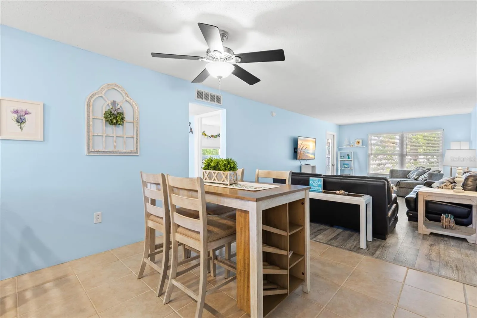 A second view of the dining area shows how naturally it opens into the living room, with tile flooring transitioning to luxury vinyl and a wide bank of windows bringing light into the far end of the space.