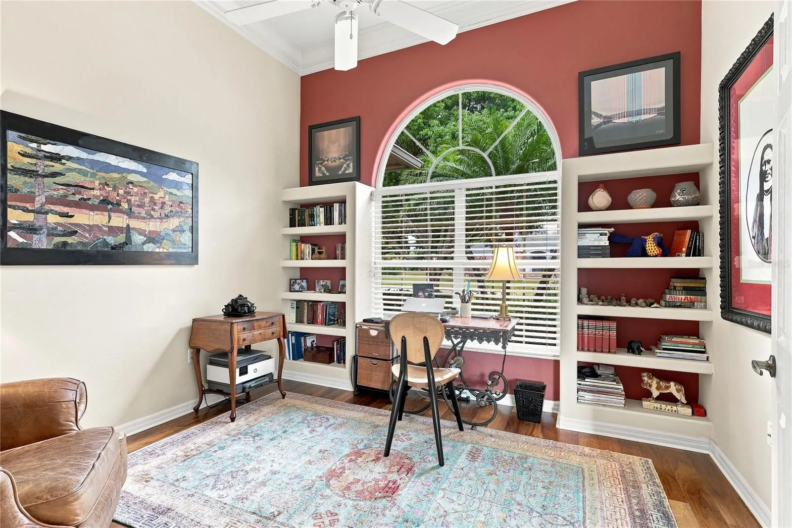 Private home office with hardwood floors, built-in shelving and a large arched window