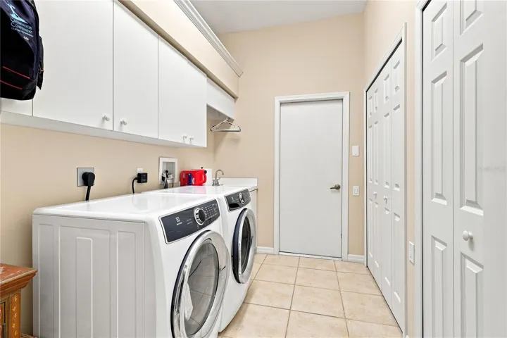 Spacious laundry room with utility sink, upper cabinetry and generous storage