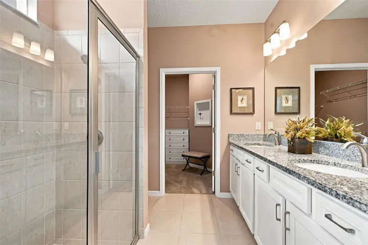 Primary en-suite bath w/walk-in tiled shower, built-in bench, transom window, granite countertop, dual vanity &amp; closet w/laundry chute door