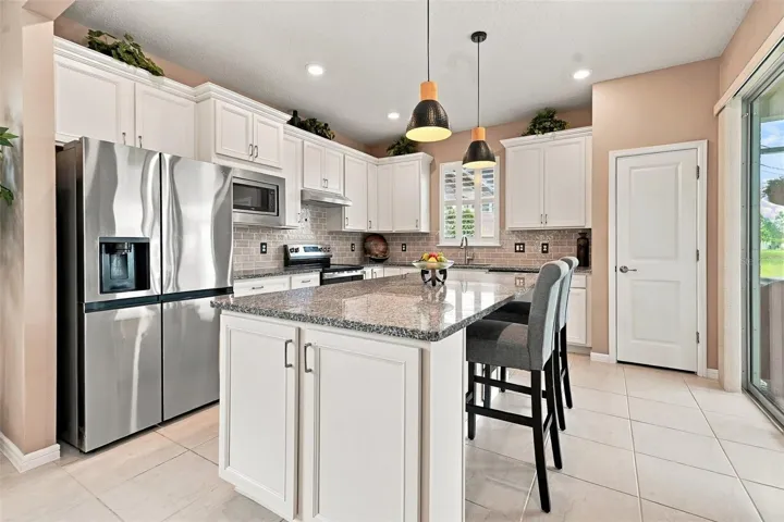 Upgraded kitchen w/granite countertops, SS appliances, tiled backsplash, pantry, center island, pendant lights, window w/shutters &amp; sliding glass door to screened lanai