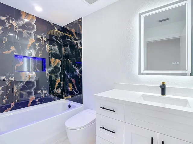 2nd bathroom features bathtub with lit cubby, smart mirror, toilet with bidet and a single vanity.
