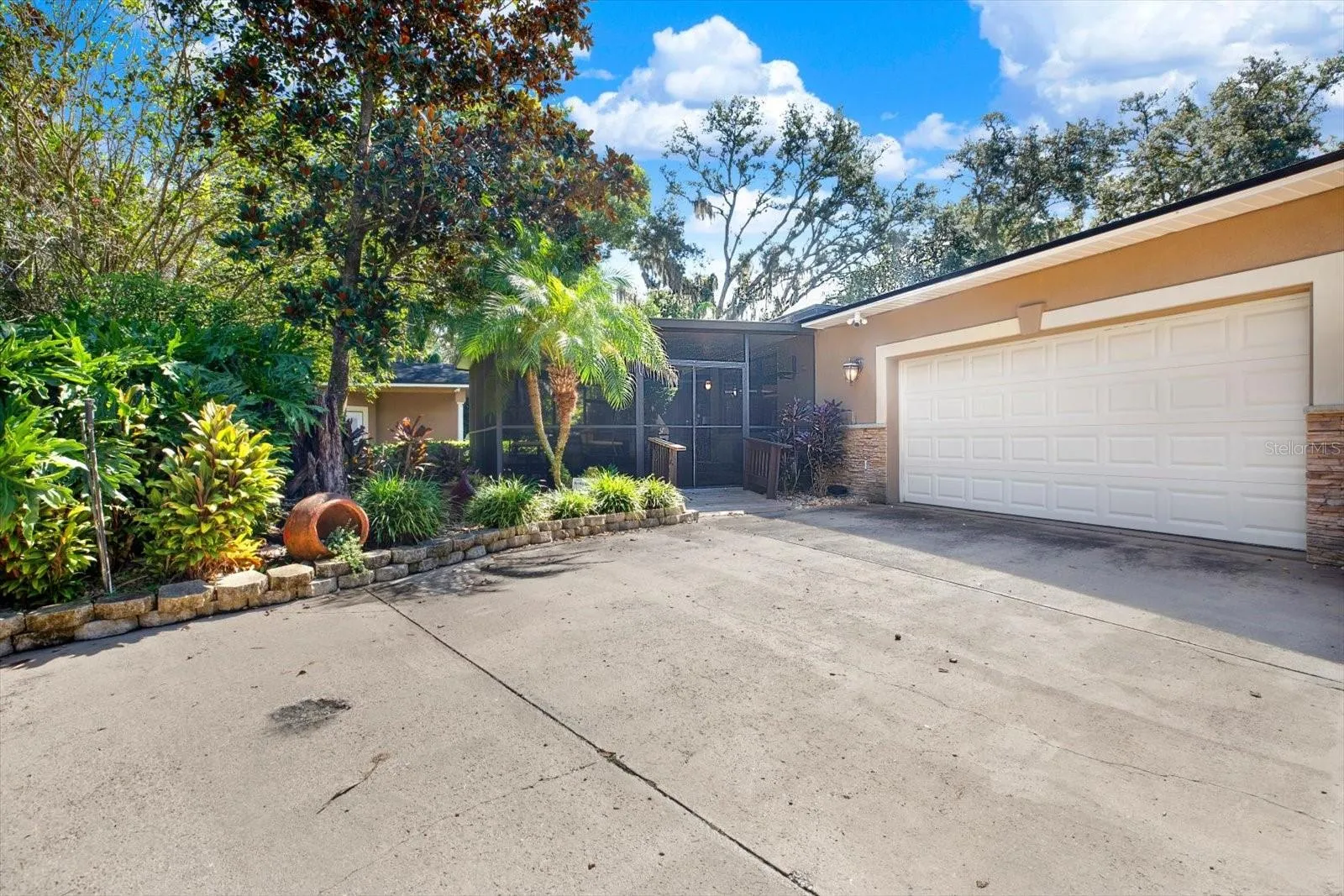 Rear wo-car garage and paver driveway with lush, mature landscaping.