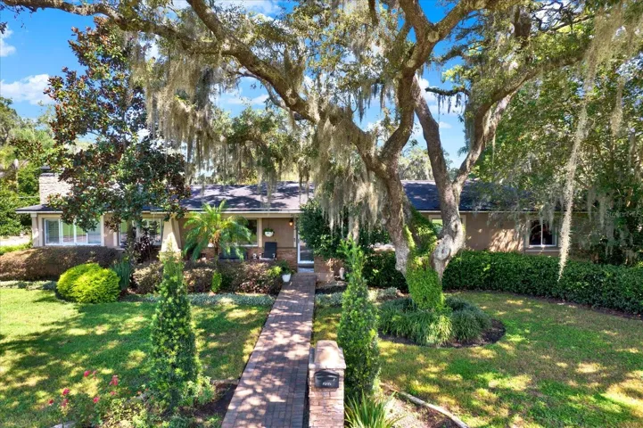 Front exterior framed by mature oak trees and Spanish moss on a private corner lot.