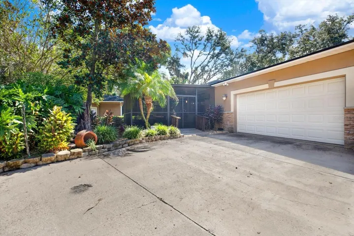 Rear wo-car garage and paver driveway with lush, mature landscaping.