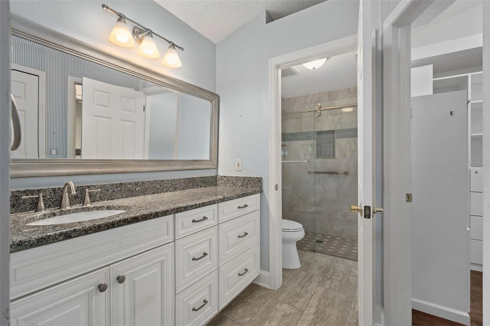 master bathroom with custom cabinetry granite countertop, custom tile on the floor and throughout the shower with a frameless shower door. Shower has also zero access with no ledge.