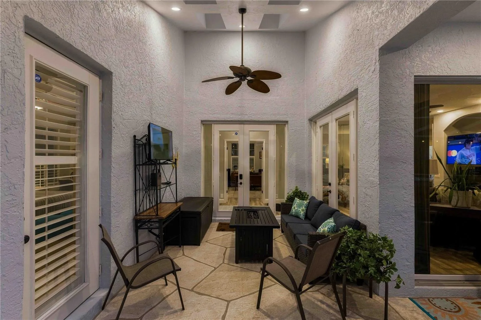 A cozy covered nook off the primary suite with a gas fire table, wall-mounted TV, and cushioned seating — the perfect spot to unwind in the evening
