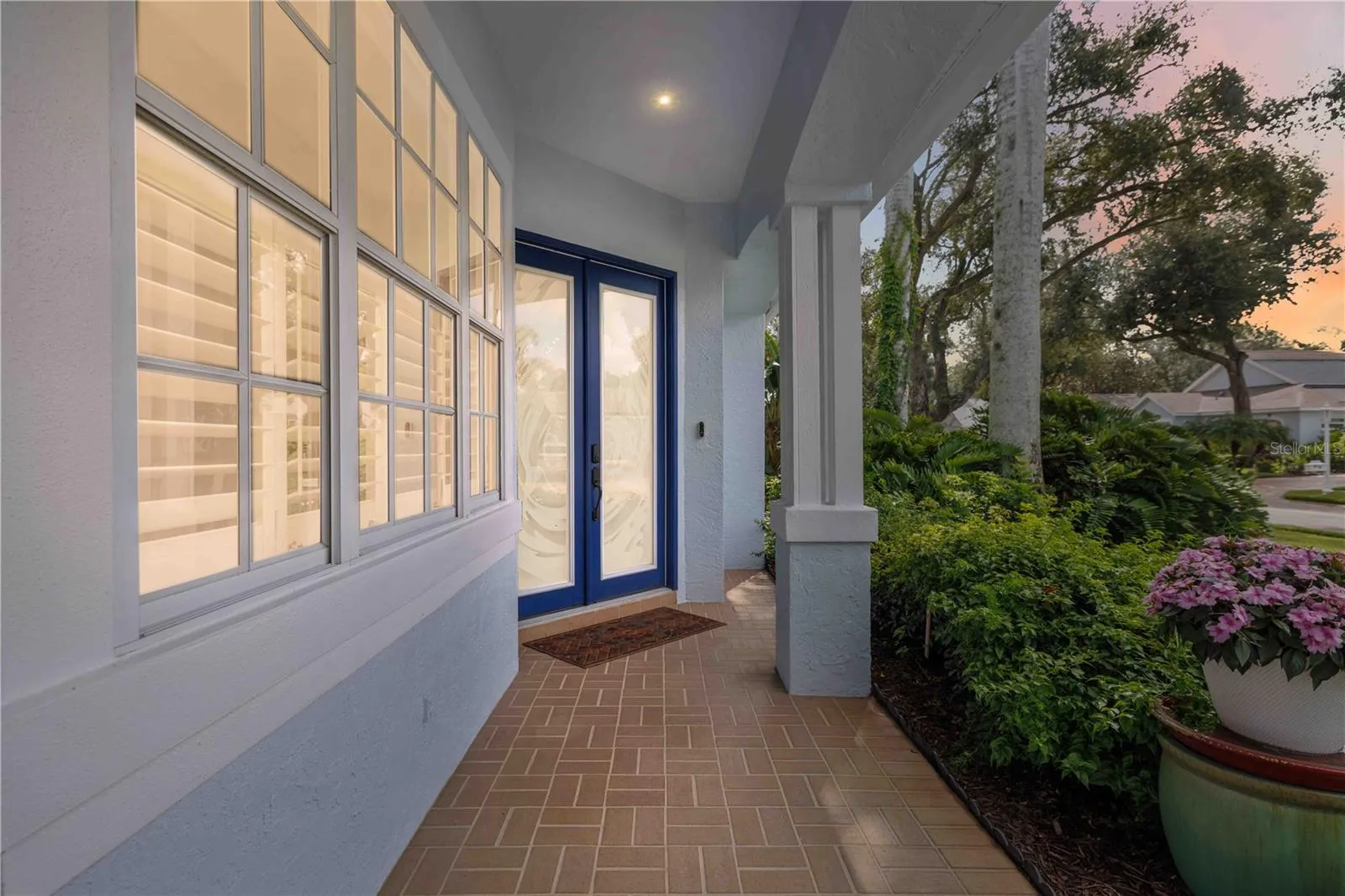 Covered front entry welcomes you in — brick paver walkway, lush landscaping, and etched glass French doors set the tone