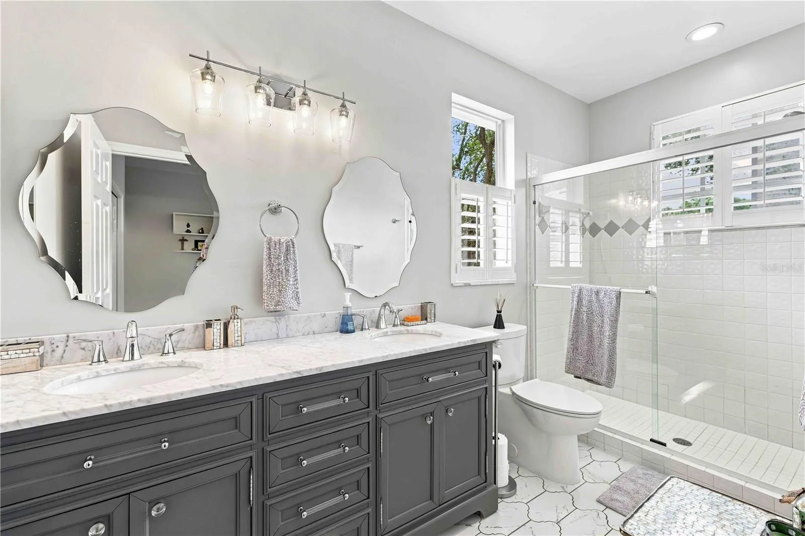 The upstairs primary bath features a dual-sink marble vanity and a glass-enclosed shower with a playful diamond tile accent