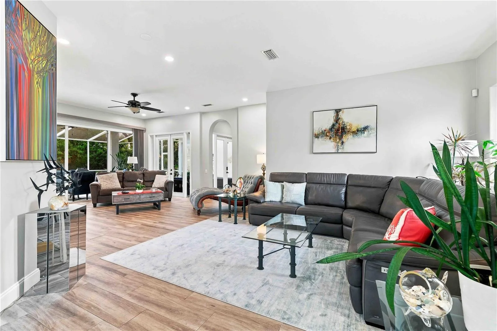 An easy, open great room with wood-look tile, custom art, and sliders out to the lanai — built for entertaining