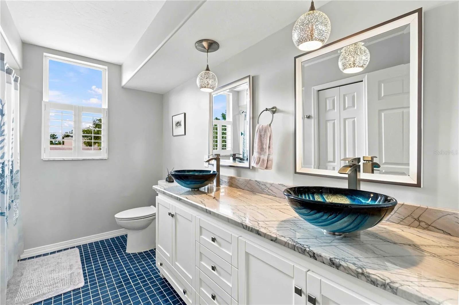 A striking guest bath with hand-blown glass vessel sinks and cobalt tile flooring — a real showstopper