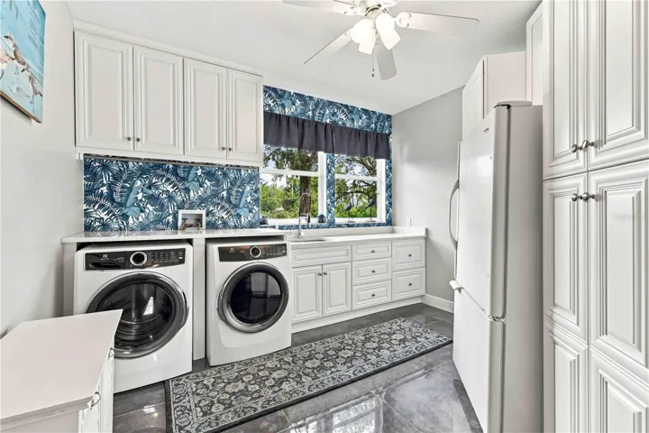 A cheerful, fully outfitted upstairs laundry room with tropical wallpaper and abundant cabinet storage.