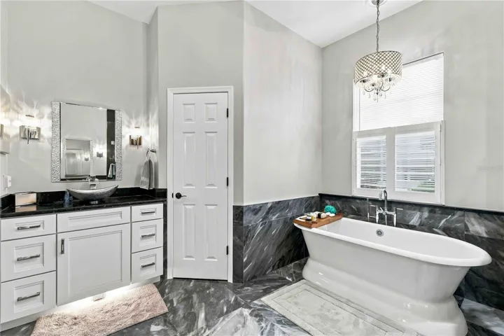 Sleek black marble and a crystal chandelier elevate this primary bath — pure luxury