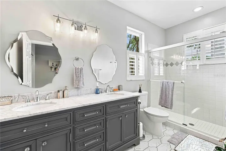The upstairs primary bath features a dual-sink marble vanity and a glass-enclosed shower with a playful diamond tile accent