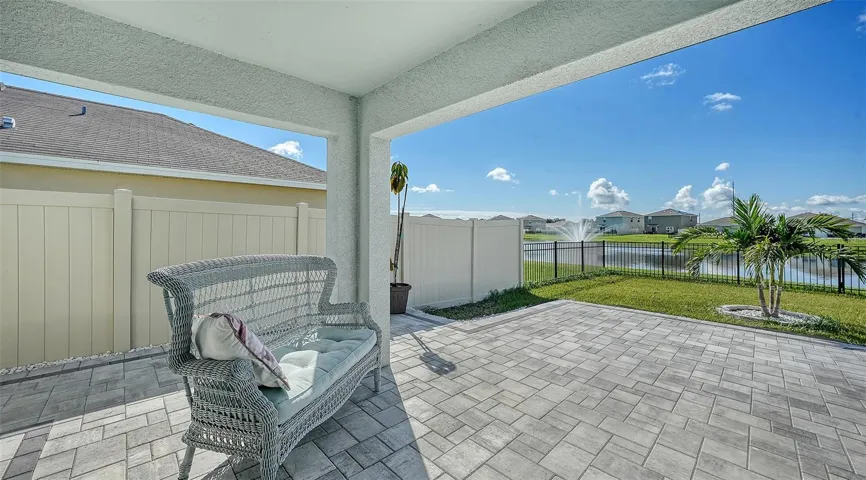 Extended lanai with patio pavers overlooking the fenced in backyard and a pretty view of the pond with a water fountain.