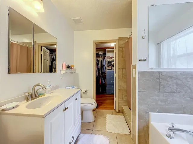 Primary bath with single sink, vanity, walk in closet, separate shower and garden tub