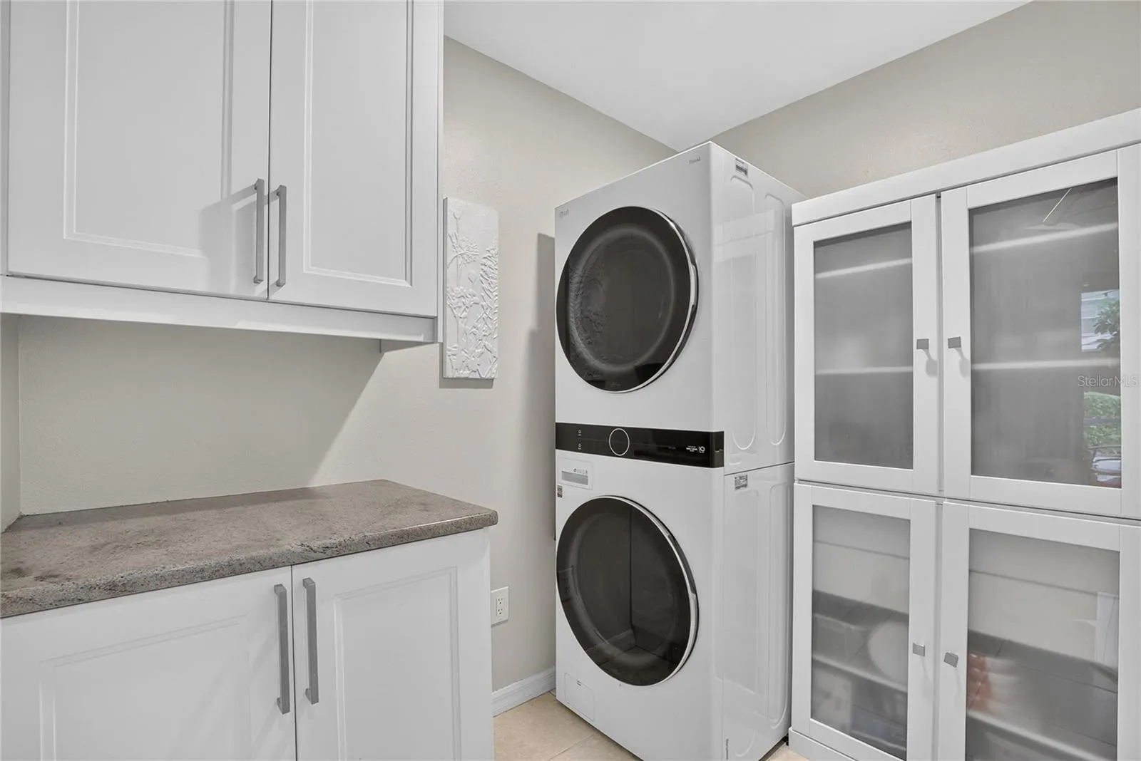 Well-appointed laundry room with stacked washer and gas dryer, abundant cabinetry, counter space and additional storage.