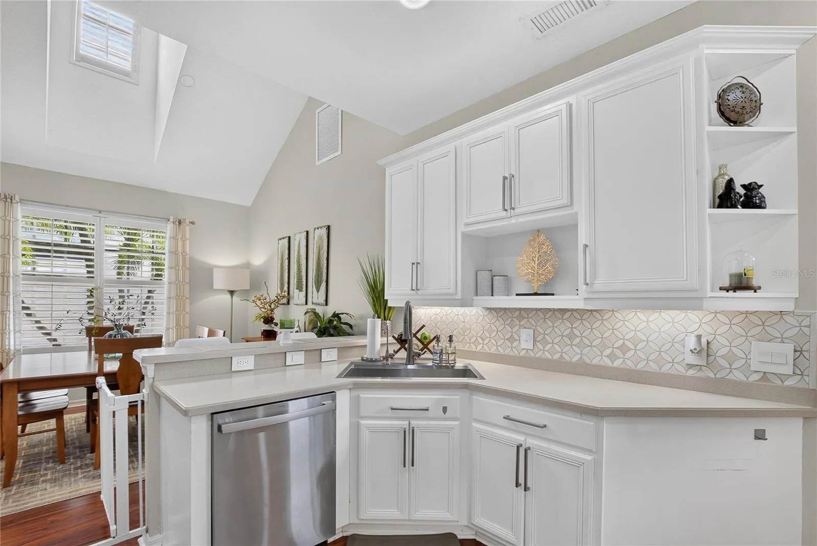 Bright, open kitchen with white cabinetry, decorative backsplash and breakfast bar overlooking the dining area.