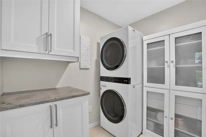 Well-appointed laundry room with stacked washer and gas dryer, abundant cabinetry, counter space and additional storage.