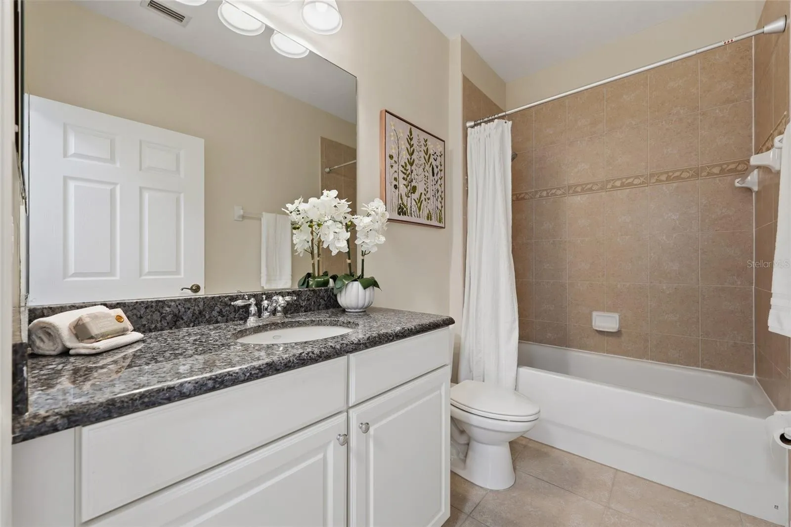 Full guest bathroom features granite countertop, white cabinetry and tiled tub/shower surround.