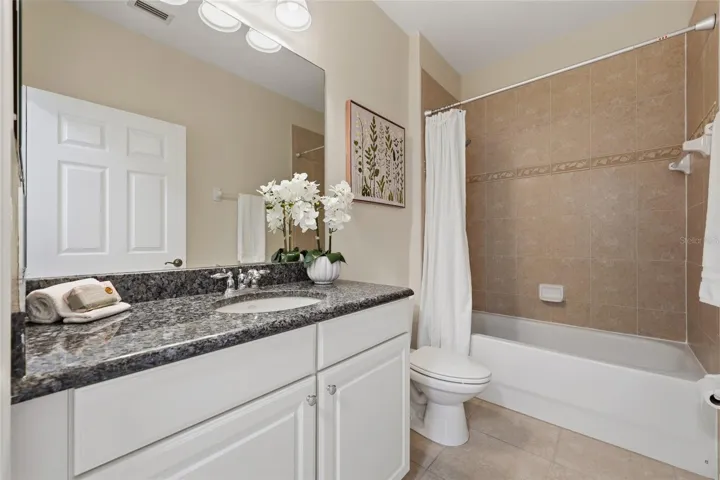 Full guest bathroom features granite countertop, white cabinetry and tiled tub/shower surround.