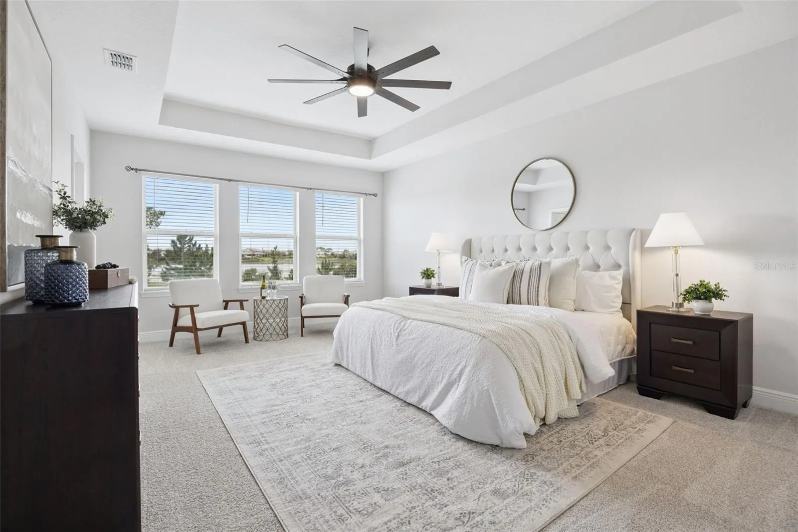 Primary bedroom with tray ceiling, ceiling fan, and pond-view windows