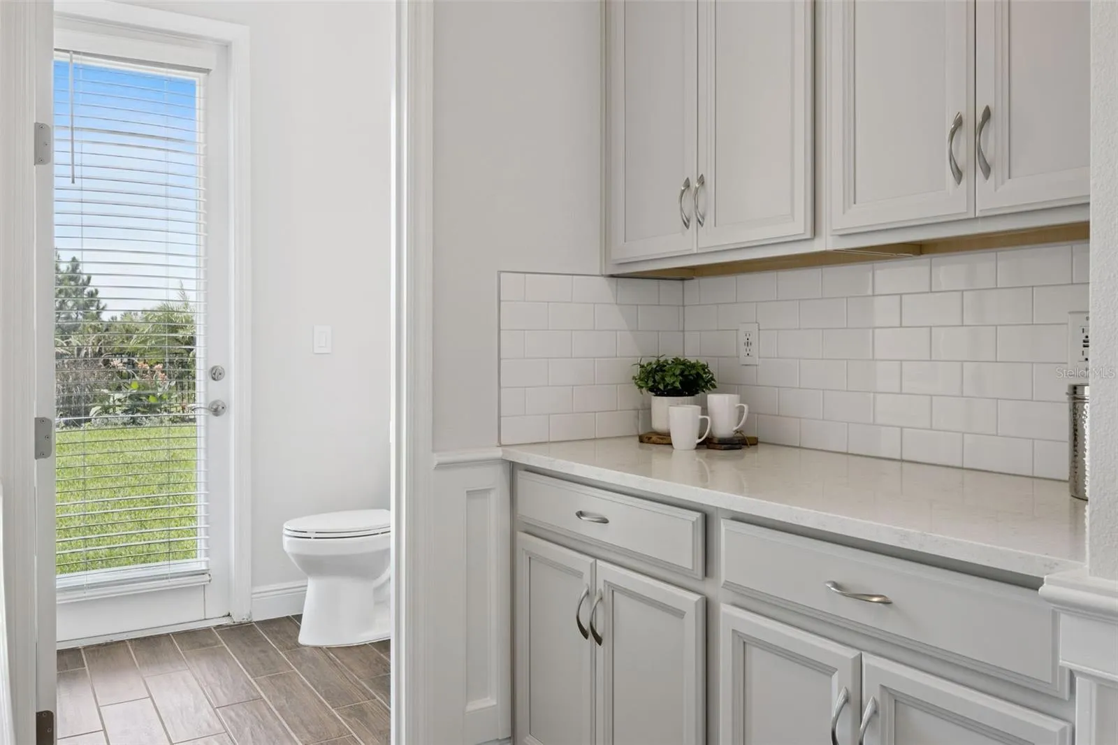 Butler's pantry with quartz counter and subway tile backsplash near the rear entry