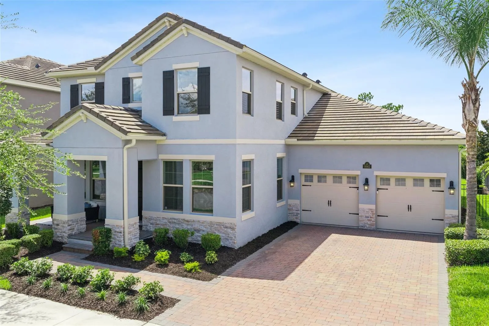 Front exterior with covered porch, brick paver driveway, and three-car garage