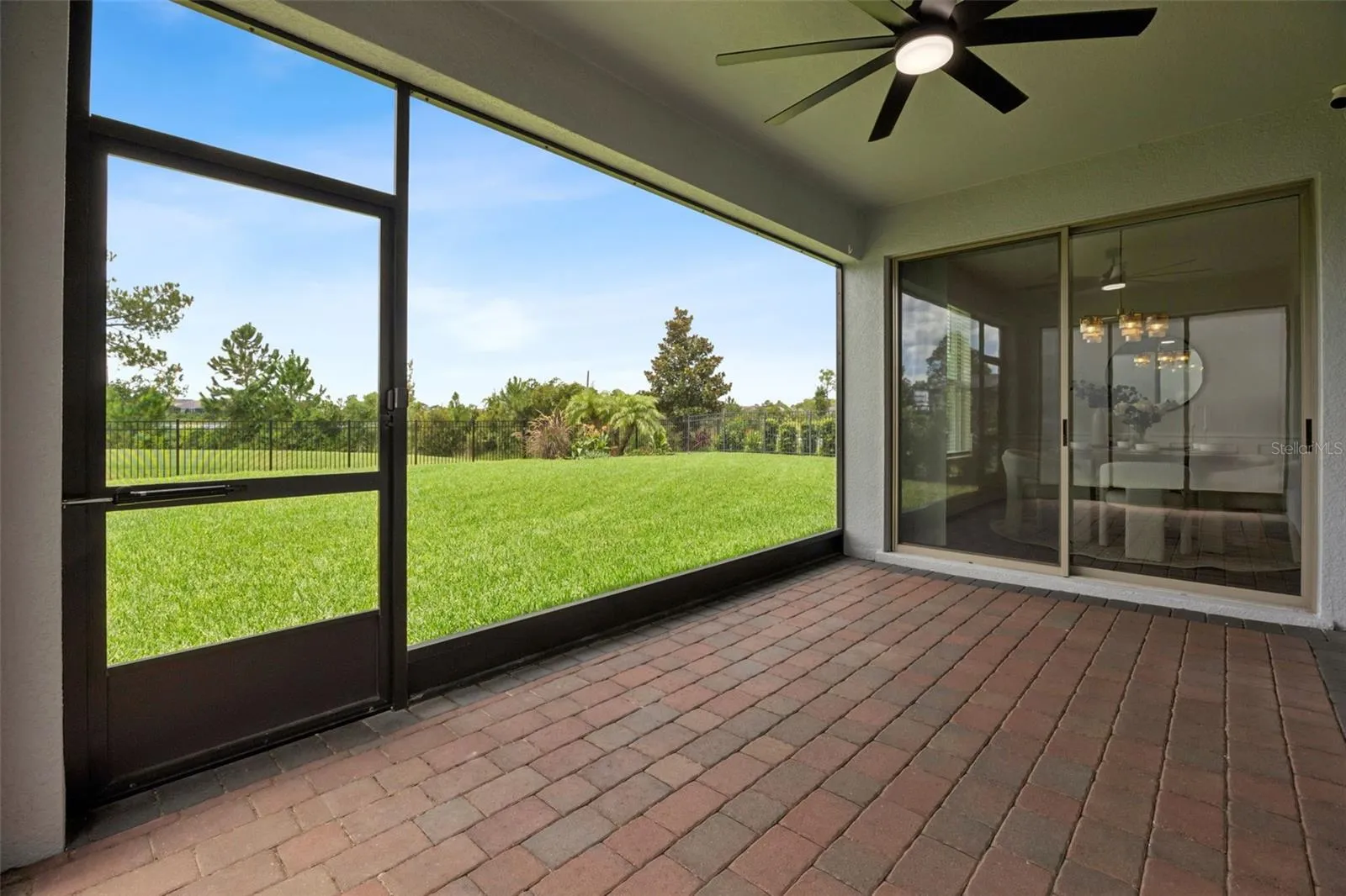 Screened lanai with brick pavers, ceiling fan, and sliding door access