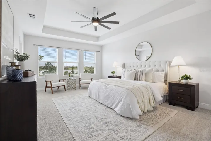 Primary bedroom with tray ceiling, ceiling fan, and pond-view windows