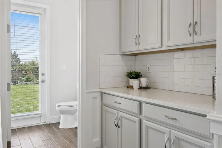 Butler's pantry with quartz counter and subway tile backsplash near the rear entry
