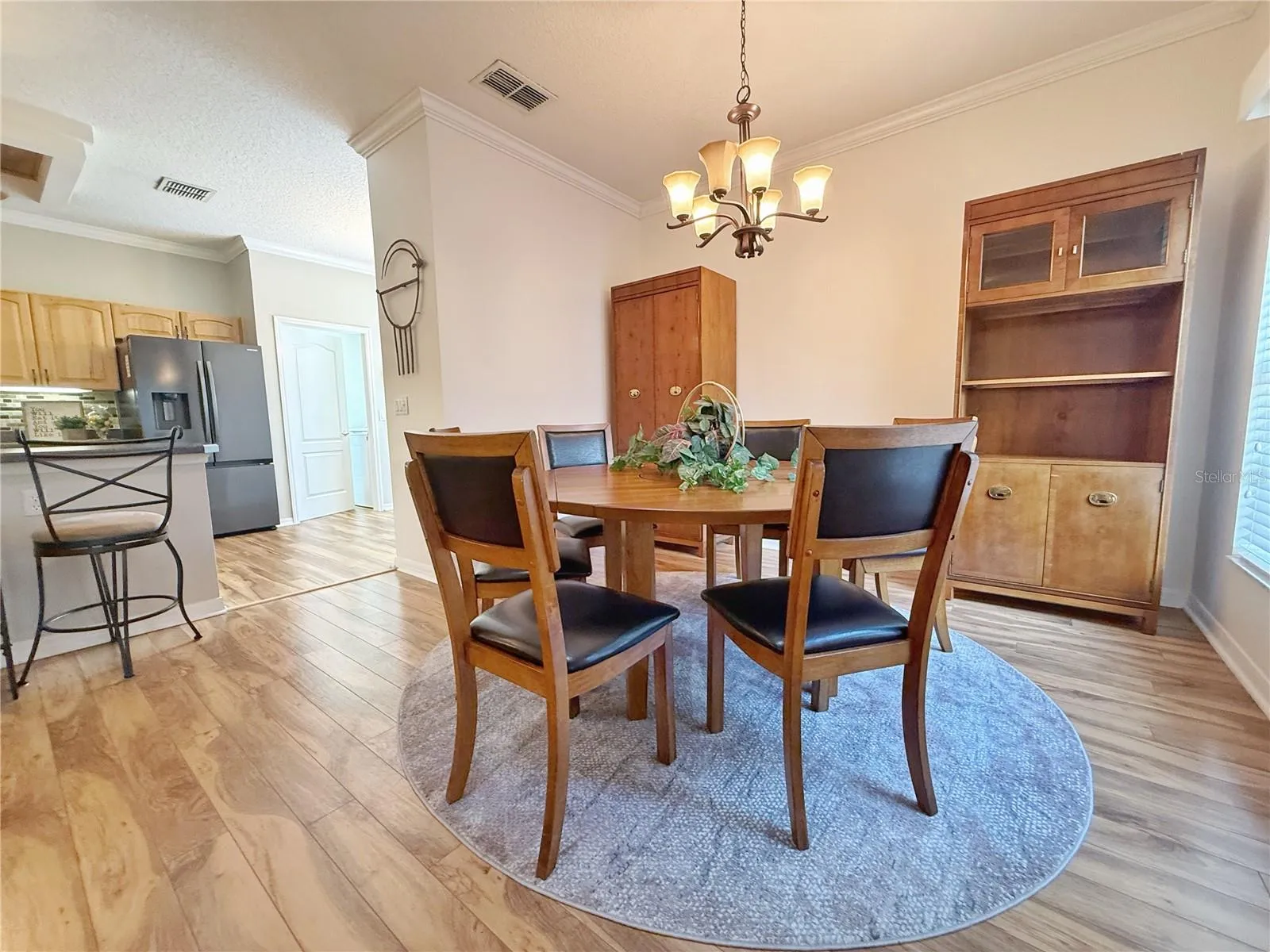 Dining room with Kitchen and bar top seating in the background. Laminate flooring, crown molding, updated fixtures and a gold course view from the window.
