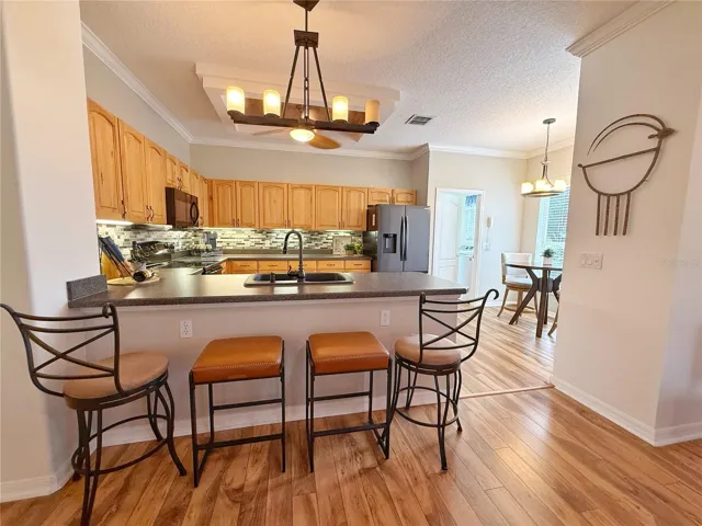 Kitchen with solid wood cabinets with under cabinet lighting, laminate flooring, crown molding, backsplash, stainless steel appliances, Dinette  and bar top seating