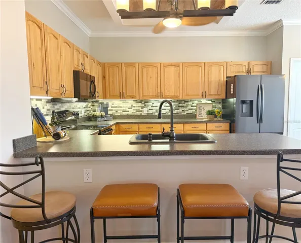Kitchen with solid wood cabinets with under cabinet lighting, stainless steel appliances,backsplash, crown molding, laminate flooring, closet pantry, dinette and bar top seating, updated fixtures