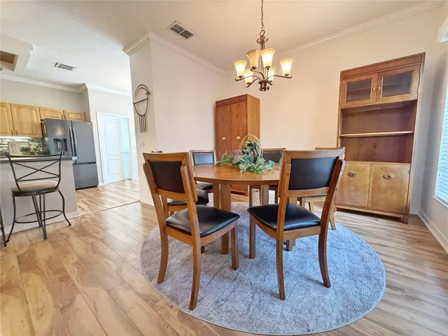Dining room with Kitchen and bar top seating in the background. Laminate flooring, crown molding, updated fixtures and a gold course view from the window.