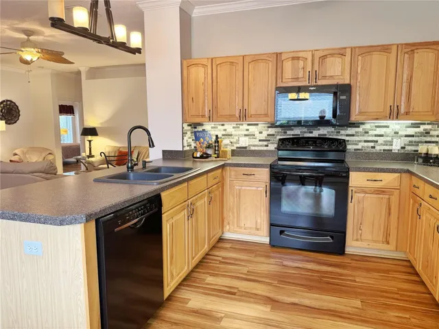 Additional Kitchen view with Living Room in background, laminate flooring, solid wood cabinets with under cabinet lighting, backsplash, black stainless steel appliances