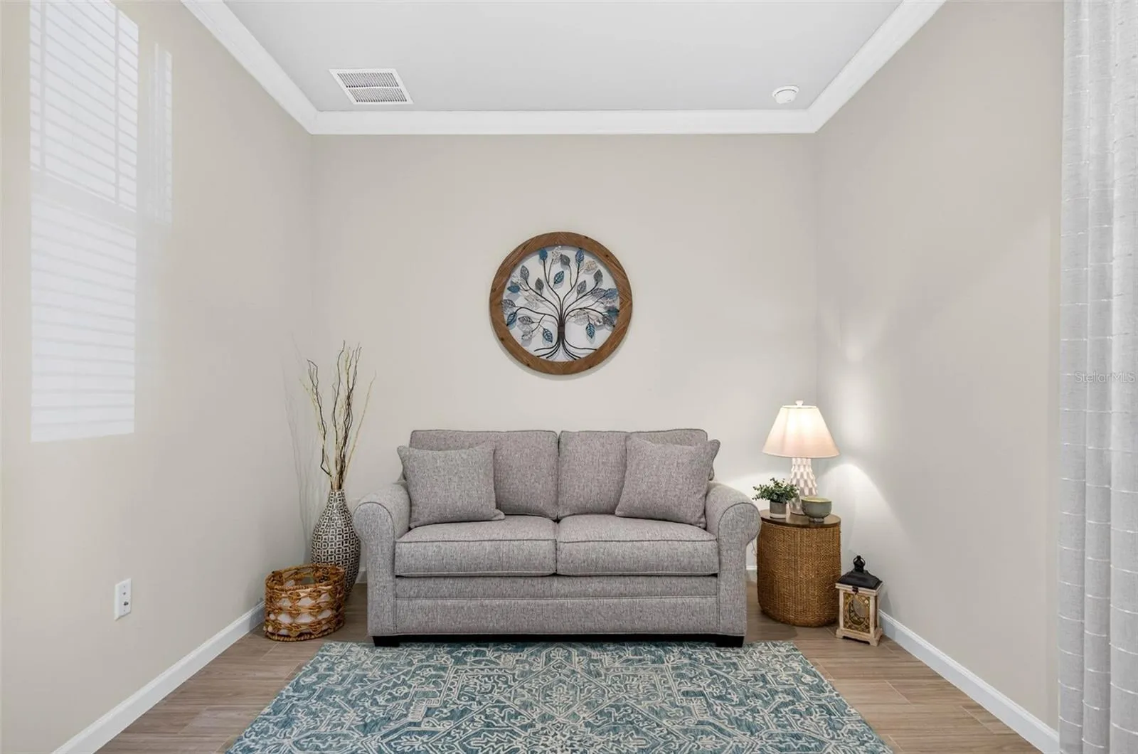 Den accented with wood-like tile flooring and crown molding in ceiling