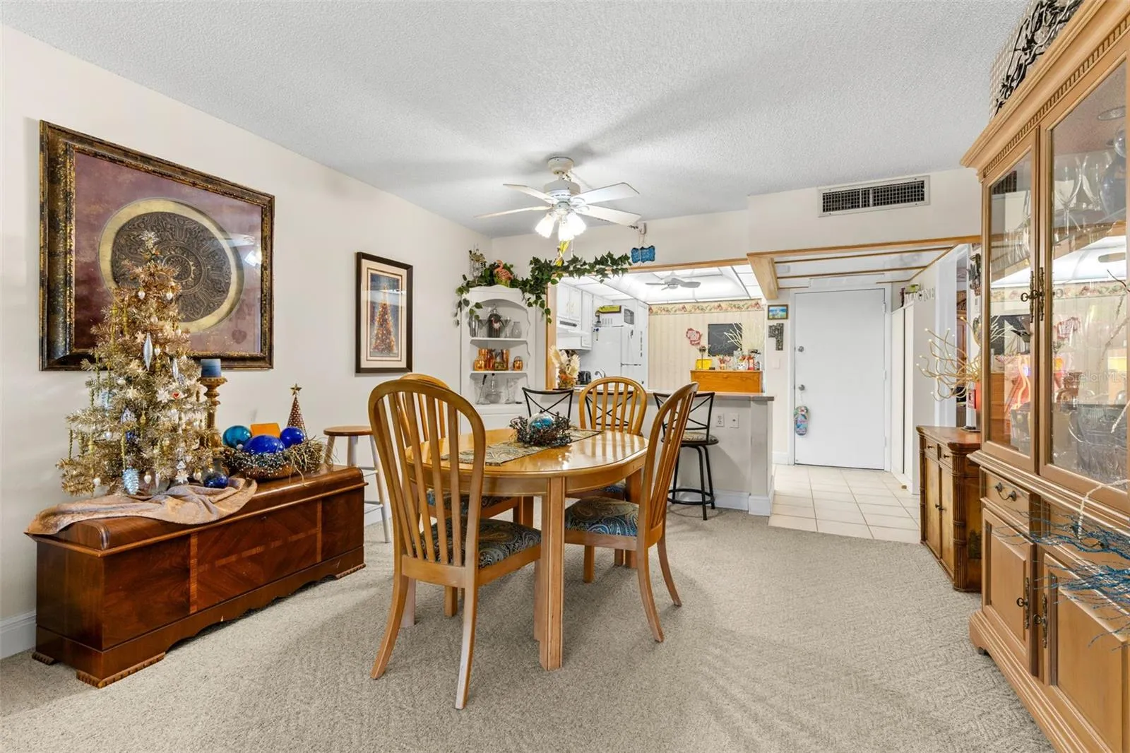 Neutral carpeting and soft wall tones keep the dining area understated, while a ceiling fan adds practical comfort. The open connection to the kitchen keeps the space visually linked without losing its own defined footprint.