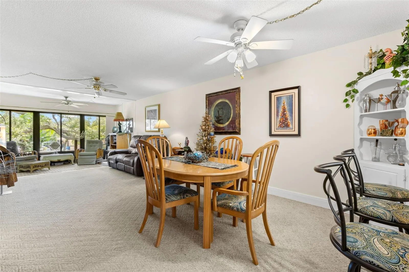 The dining area sits between the kitchen and living room, creating a long, open main living space with plenty of room to define each area. A wall of windows at the far end brings in natural light and looks out toward the trees and landscaped grounds.